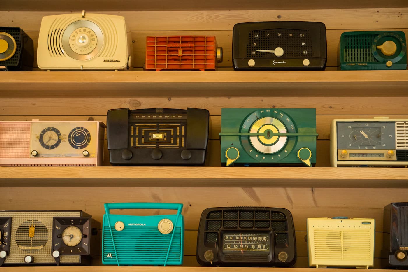 A collection of colorful vintage radios on wooden shelves